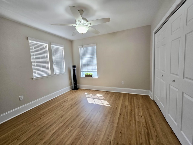 unfurnished bedroom with baseboards, a closet, wood finished floors, and a ceiling fan
