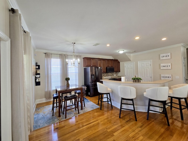 kitchen with light wood-style flooring, refrigerator with ice dispenser, stainless steel microwave, a breakfast bar area, and a notable chandelier