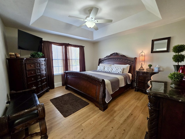 bedroom with light wood finished floors, ceiling fan, and a raised ceiling
