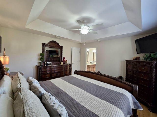 bedroom with visible vents, connected bathroom, wood finished floors, a ceiling fan, and a tray ceiling