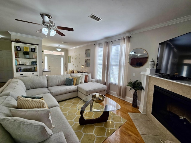 living room featuring crown molding, baseboards, visible vents, ceiling fan, and wood finished floors