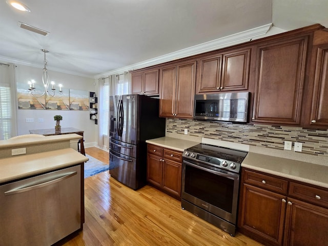 kitchen with light countertops, an inviting chandelier, stainless steel appliances, hanging light fixtures, and light wood-style flooring