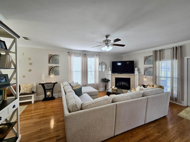 living room featuring dark wood-style flooring, a tile fireplace, visible vents, ceiling fan, and ornamental molding