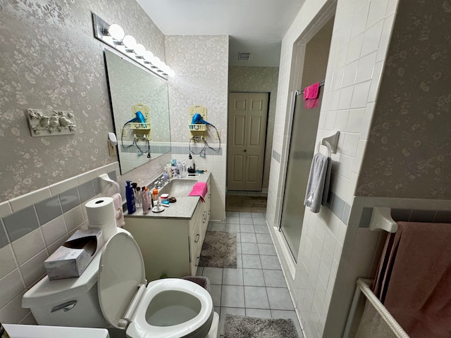 bathroom with vanity, a shower with door, tile patterned floors, toilet, and tile walls