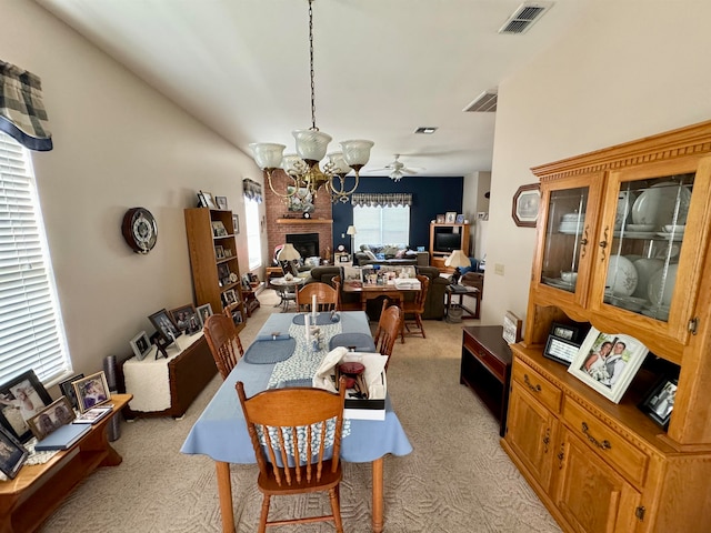 dining area with light carpet, a fireplace, and ceiling fan with notable chandelier