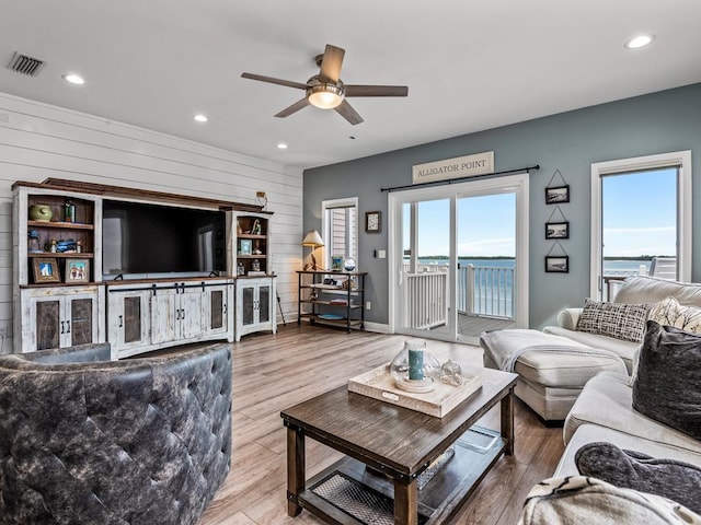 living room featuring ceiling fan, a water view, wooden walls, and hardwood / wood-style flooring