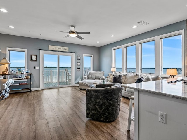 living room with ceiling fan, light hardwood / wood-style flooring, a water view, and plenty of natural light