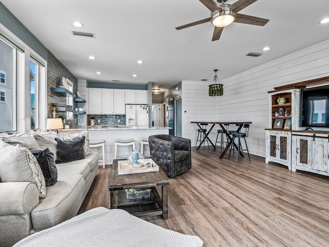 living room featuring ceiling fan, light hardwood / wood-style flooring, and wooden walls