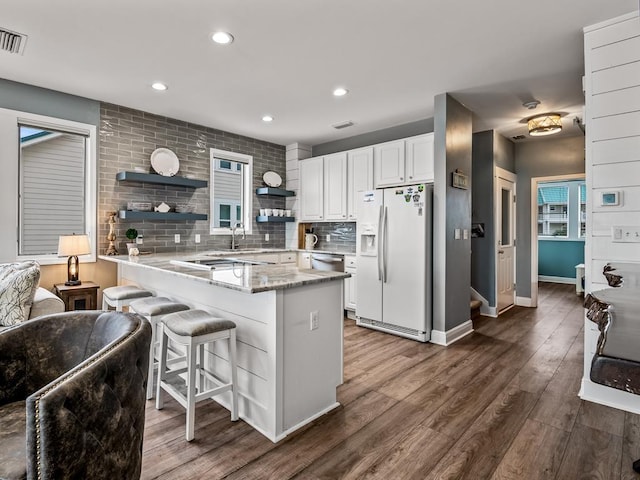 kitchen with sink, white cabinets, a kitchen breakfast bar, backsplash, and white refrigerator with ice dispenser