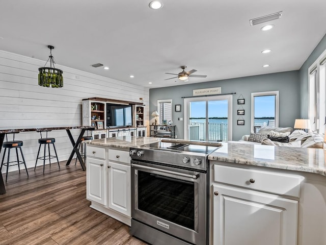 kitchen with ceiling fan, dark wood-type flooring, wooden walls, stainless steel range with electric stovetop, and white cabinetry