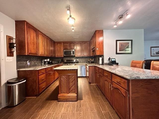 kitchen featuring appliances with stainless steel finishes, backsplash, kitchen peninsula, light stone countertops, and dark wood-type flooring