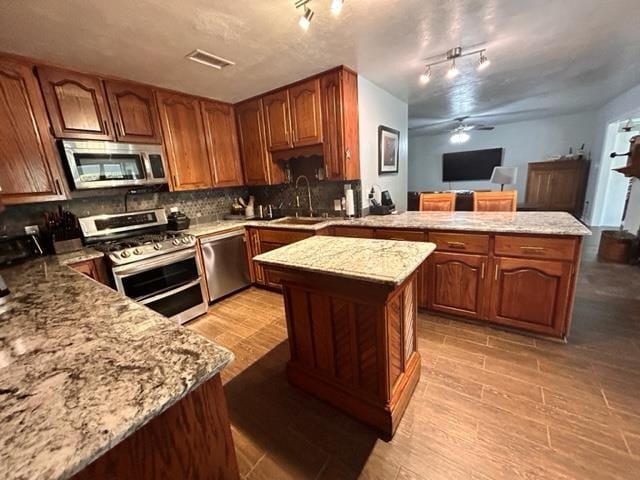 kitchen with light stone counters, tasteful backsplash, appliances with stainless steel finishes, kitchen peninsula, and a kitchen island