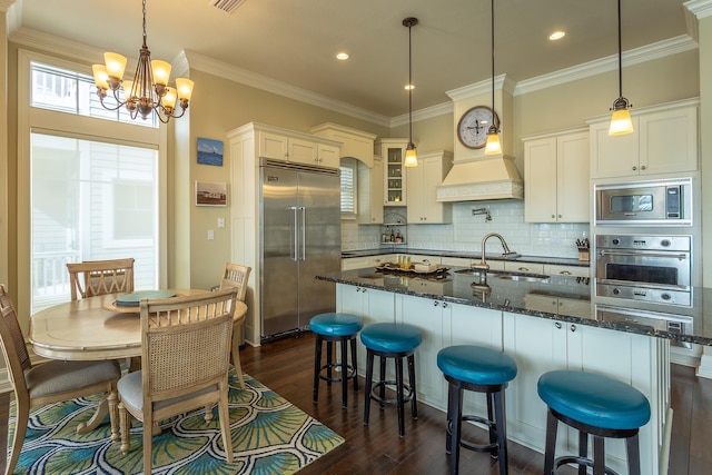 kitchen with pendant lighting, sink, built in appliances, white cabinets, and dark stone counters