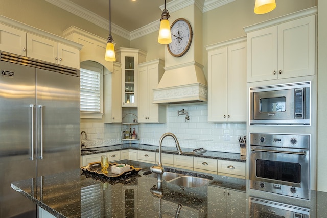 kitchen with sink, built in appliances, tasteful backsplash, decorative light fixtures, and dark stone counters