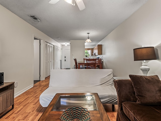 living area with visible vents, light wood-type flooring, a ceiling fan, and baseboards