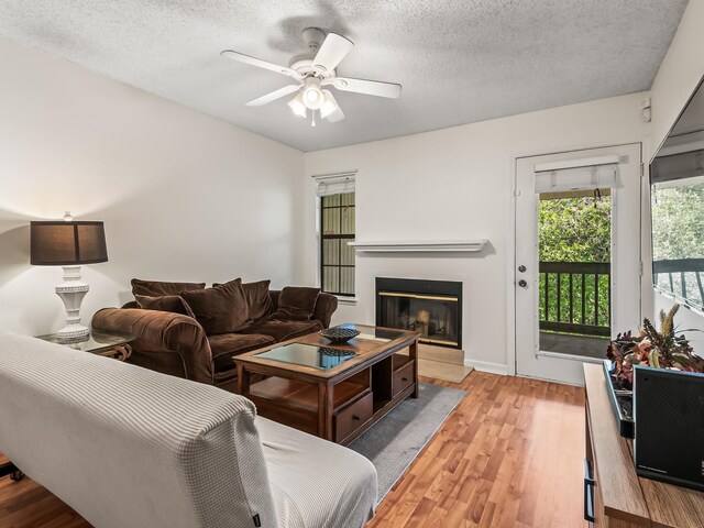 living room featuring a glass covered fireplace, wood finished floors, a ceiling fan, and a textured ceiling