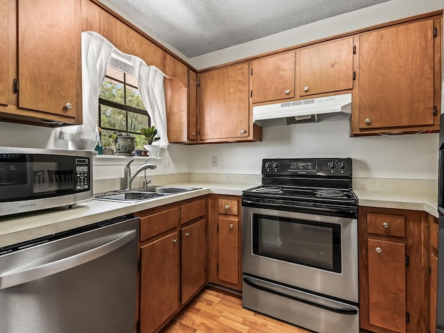 kitchen featuring appliances with stainless steel finishes, a sink, light countertops, and under cabinet range hood