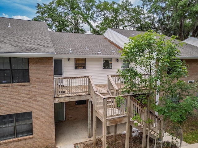 rear view of house featuring a deck, brick siding, stairs, and roof with shingles