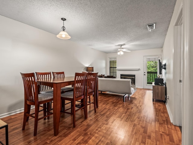dining area with a textured ceiling, baseboards, a glass covered fireplace, wood finished floors, and a ceiling fan
