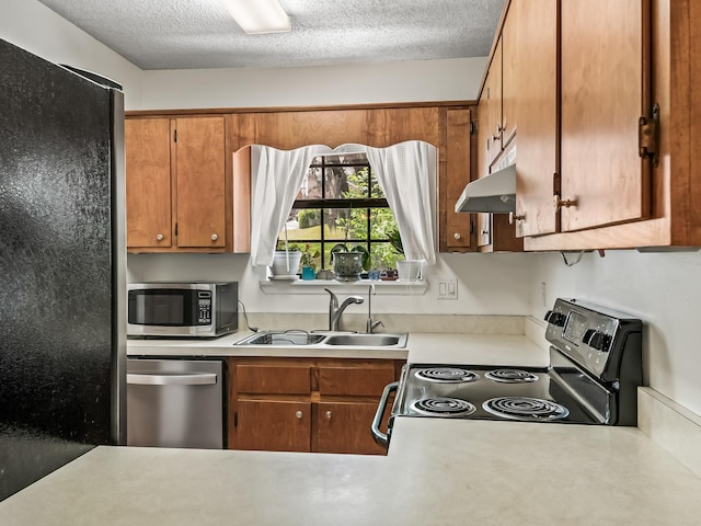 kitchen with stainless steel appliances, under cabinet range hood, light countertops, and a sink