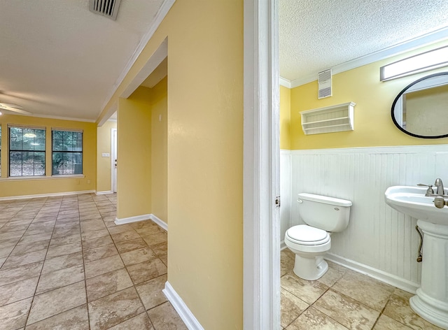 bathroom featuring sink, crown molding, ceiling fan, toilet, and a textured ceiling