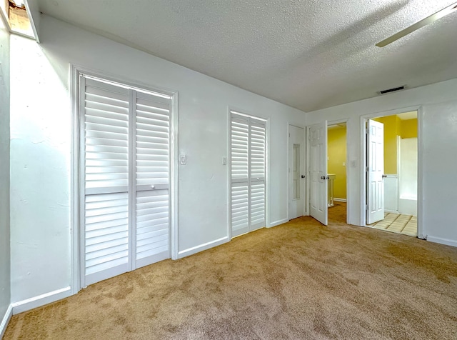 unfurnished bedroom with light carpet, ceiling fan, ensuite bathroom, and a textured ceiling