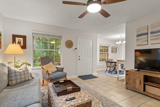 living room with light tile patterned floors, a textured ceiling, baseboards, and ceiling fan with notable chandelier