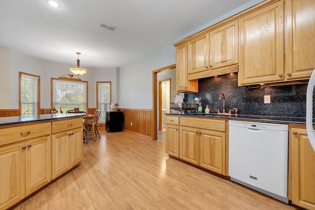 kitchen featuring white dishwasher, a sink, dark countertops, light brown cabinetry, and wainscoting