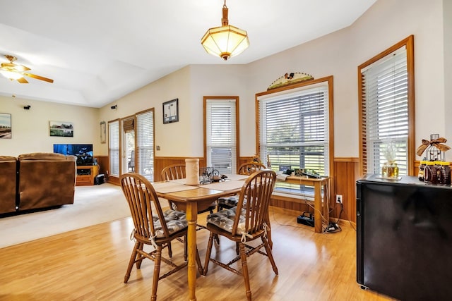 dining room with wooden walls, light wood-style floors, a wainscoted wall, and ceiling fan