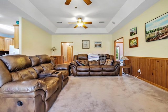 living room with a ceiling fan, wood walls, visible vents, a tray ceiling, and wainscoting