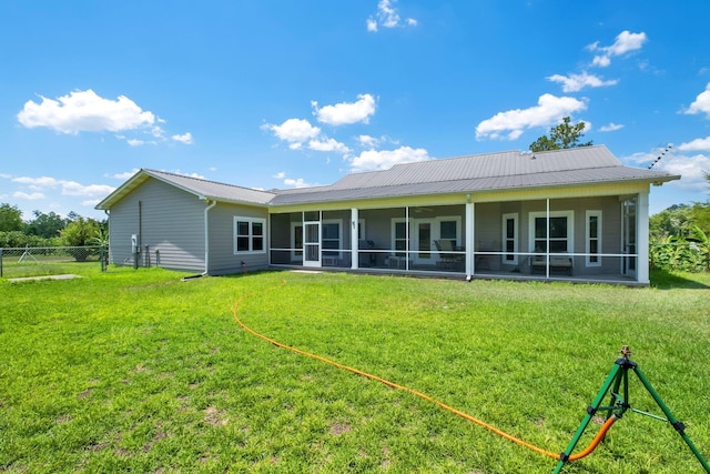rear view of property with fence, metal roof, a sunroom, and a lawn