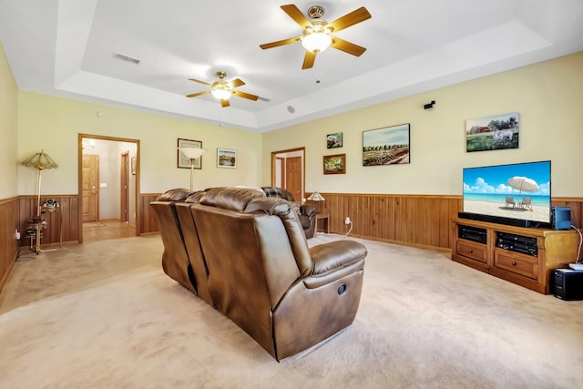 living area with light carpet, wainscoting, a tray ceiling, visible vents, and ceiling fan