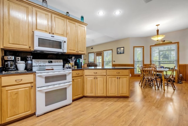 kitchen featuring light brown cabinets, dark countertops, white appliances, a peninsula, and a wainscoted wall