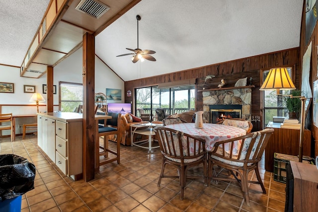 dining room with a fireplace, wood walls, ceiling fan, tile patterned floors, and a textured ceiling