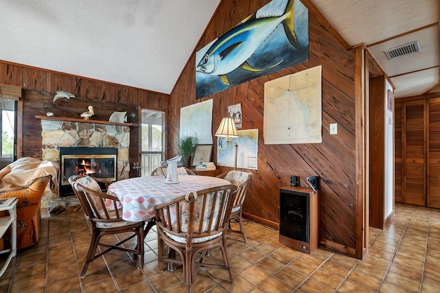 dining room featuring plenty of natural light, wooden walls, lofted ceiling, and a fireplace