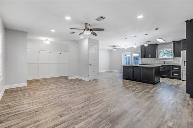 kitchen with visible vents, open floor plan, dark cabinets, a center island, and light wood-style floors