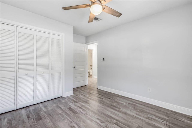 unfurnished bedroom featuring baseboards, visible vents, a ceiling fan, wood finished floors, and a closet