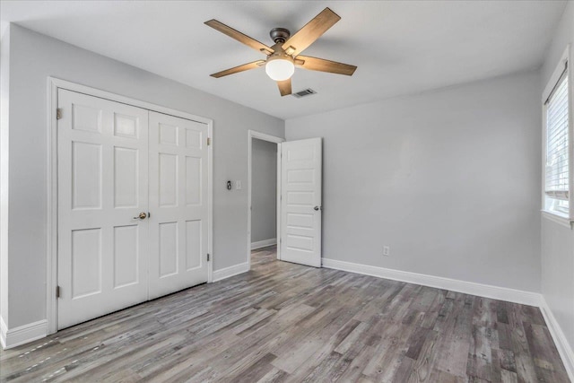 unfurnished bedroom with a closet, wood finished floors, visible vents, and baseboards