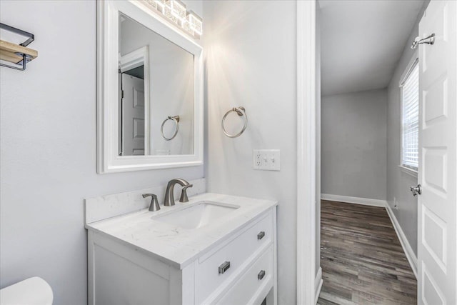 half bathroom with toilet, baseboards, wood finished floors, and vanity