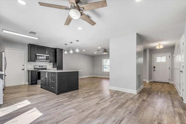 kitchen featuring stainless steel appliances, light countertops, dark cabinetry, and light wood finished floors