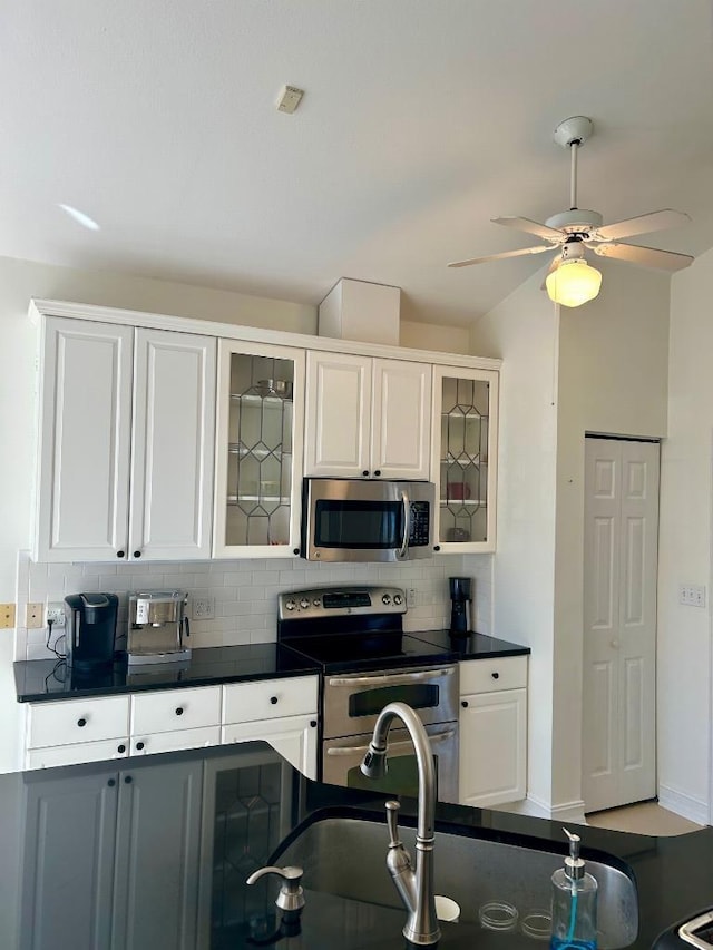 kitchen featuring tasteful backsplash, dark countertops, stainless steel appliances, white cabinets, and ceiling fan