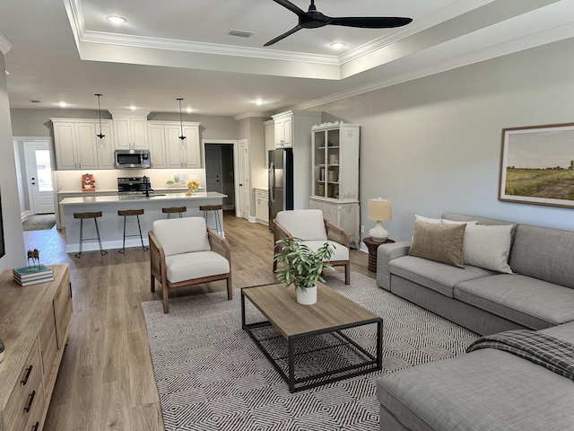 living room with ceiling fan, ornamental molding, a tray ceiling, and light hardwood / wood-style flooring