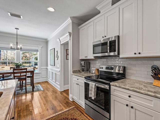 kitchen with white cabinetry, hanging light fixtures, ornamental molding, stainless steel appliances, and light stone countertops