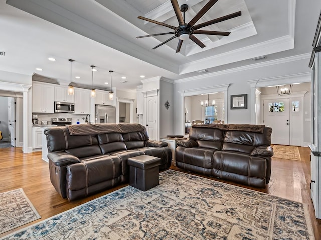 living room featuring ceiling fan with notable chandelier, ornamental molding, a raised ceiling, and light hardwood / wood-style floors