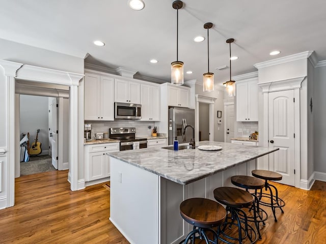 kitchen featuring appliances with stainless steel finishes, decorative light fixtures, white cabinets, a kitchen island with sink, and light stone counters