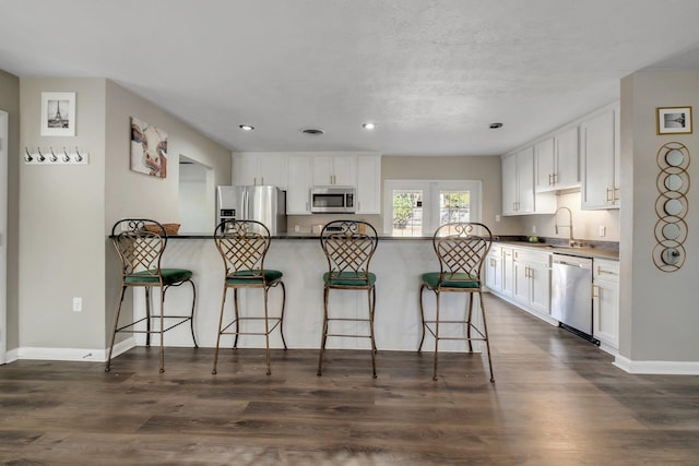 kitchen with appliances with stainless steel finishes, dark countertops, a sink, and white cabinetry