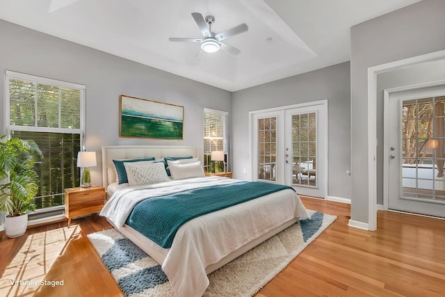 bedroom featuring ceiling fan, a tray ceiling, wood-type flooring, access to outside, and french doors