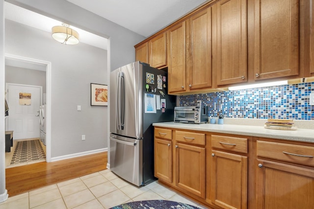 kitchen featuring backsplash, light tile patterned floors, stainless steel fridge, and washing machine and dryer