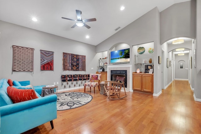 living room featuring a tiled fireplace, ceiling fan, high vaulted ceiling, and light wood-type flooring