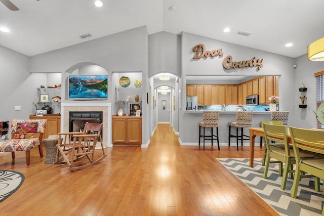 interior space featuring vaulted ceiling, light wood-type flooring, appliances with stainless steel finishes, kitchen peninsula, and a tiled fireplace